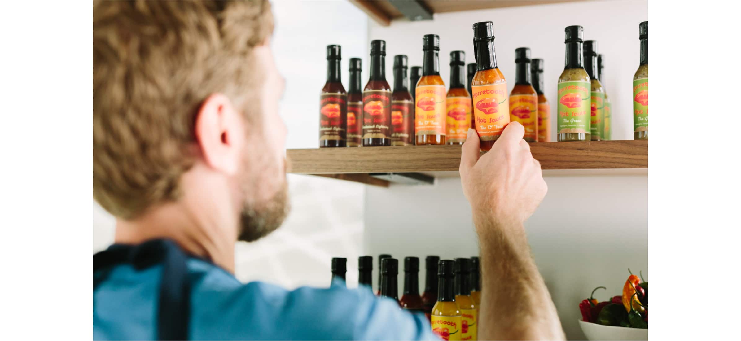 John grabbing a small sauce bottle from a shelf lined with many others.